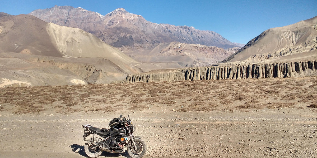 Black motorcycle parked on a gravel track below arid Himalayan mountains in Nepal