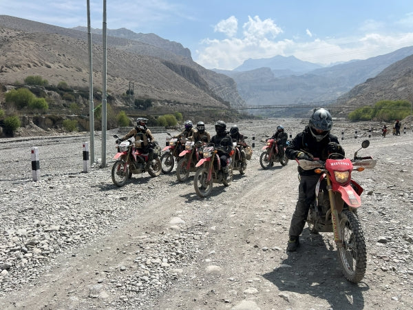 Riders on a gravel riverbed track beneath arid mountains