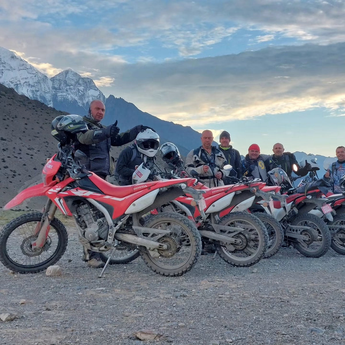 Riders and Honda CRF motorcycles in front of snow-covered mountains